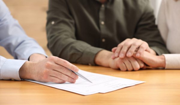 Notary showing senior couple where to sign Last Will and Testament at wooden table indoors, closeup